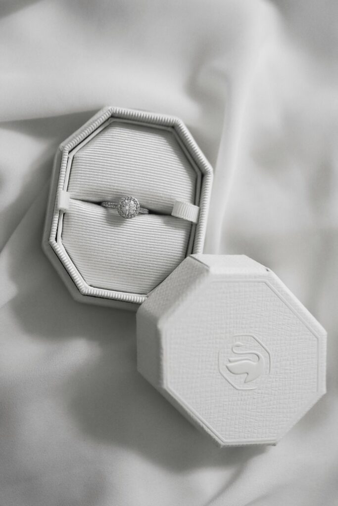 Closeup of a diamond engagement ring in an octagonal velvet box on a white fabric.